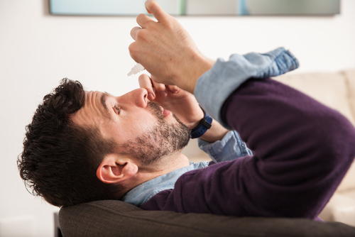 man sitting on couch and putting in eye drops